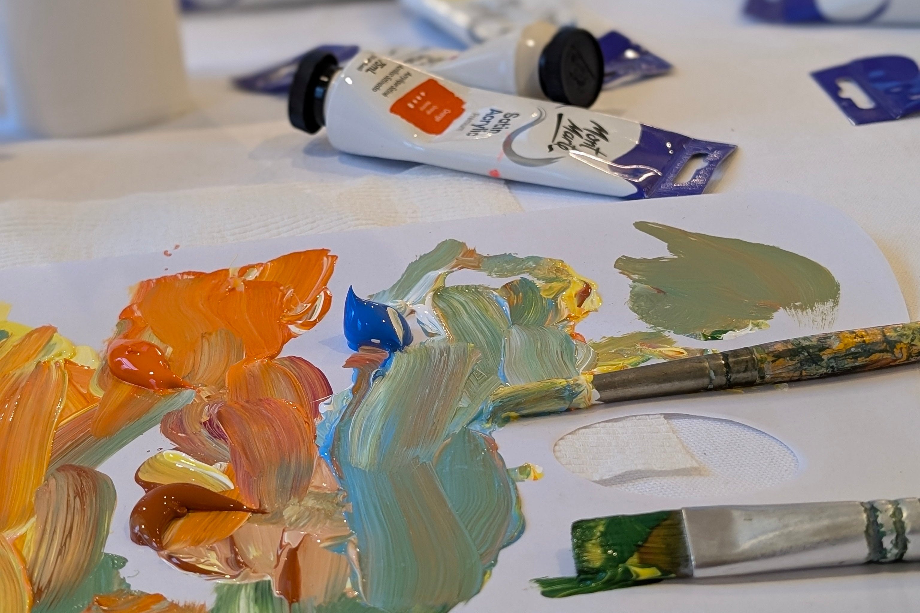 Artistic painting of flowers with paint tubes and a brush on a table.