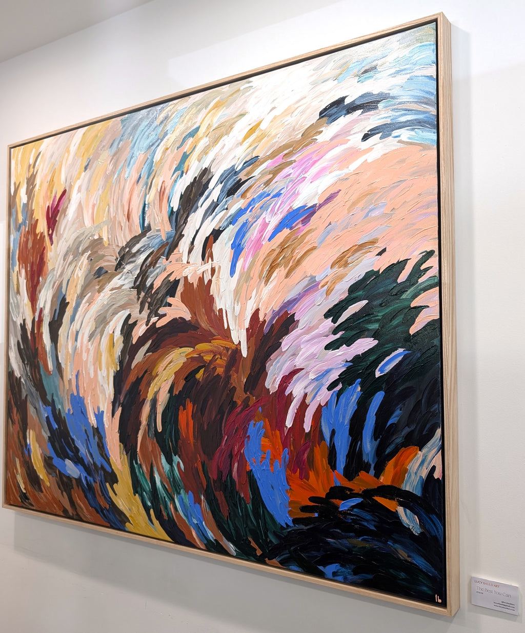 Bold statement texture abstract painting hanging on a wall with energetic but calm colors of red, blue, neutral earthy tones in an oak frame