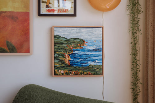 Small blue and green abstract painting of Bruny Island's coastline by Lucy Bauld hanging above a chair in a loungeroom. 